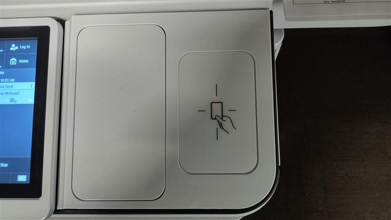 Image of the badge scanner on the printer, located to the right of the touchscreen display. On the badge scanning area is the symbol of a hand holding a rectangular badge.