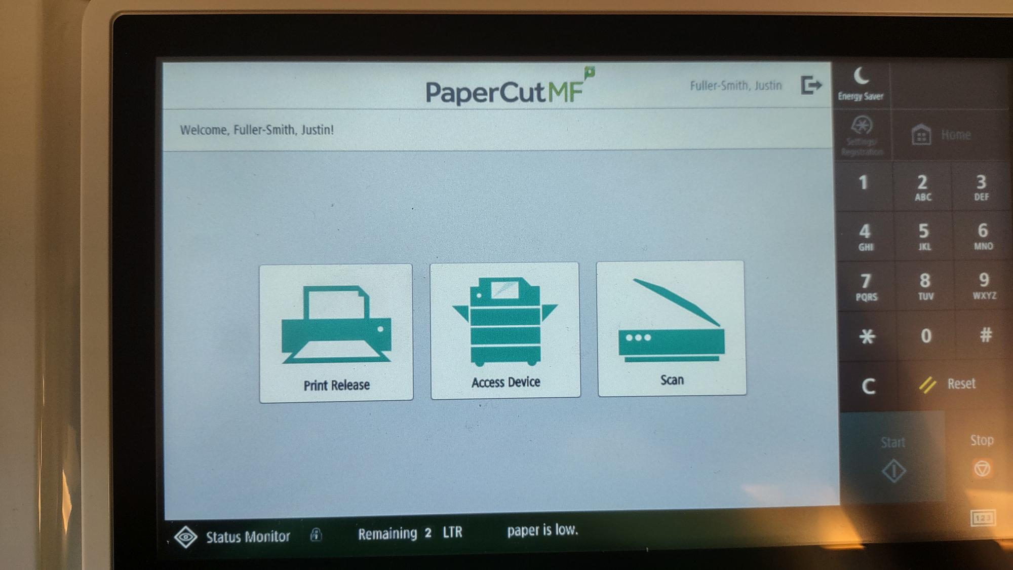 Image of the printer's touchscreen display. Three prominent buttons appear. From left to right, they are: "Print Release," "Access Device," and "Scan."